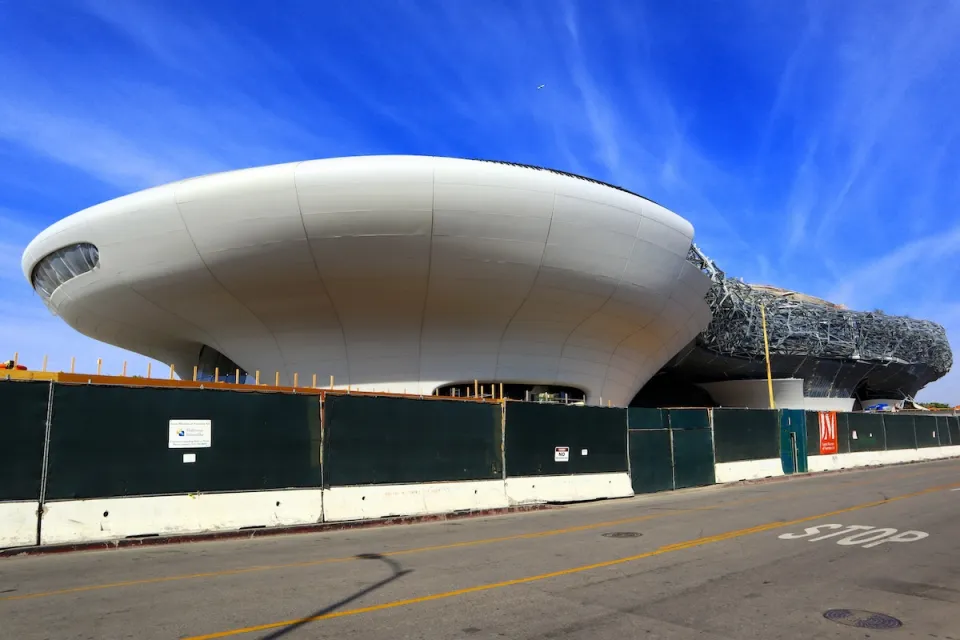 Amorphous white building for Lucas Museum of Narrative Art in Los Angeles, California under construction behind green construction fence.